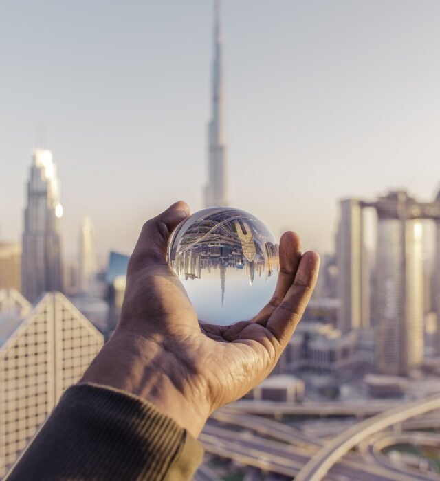 A closeup shot of a male hand holding a crystal ball with the reflection of the city